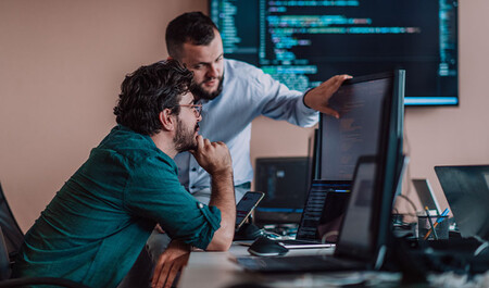Two developers reviewing code on monitor displaying security scanning visualization and metrics