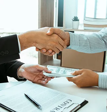 Two business professionals shaking hands and exchanging cash money over signed loan contract agreement document