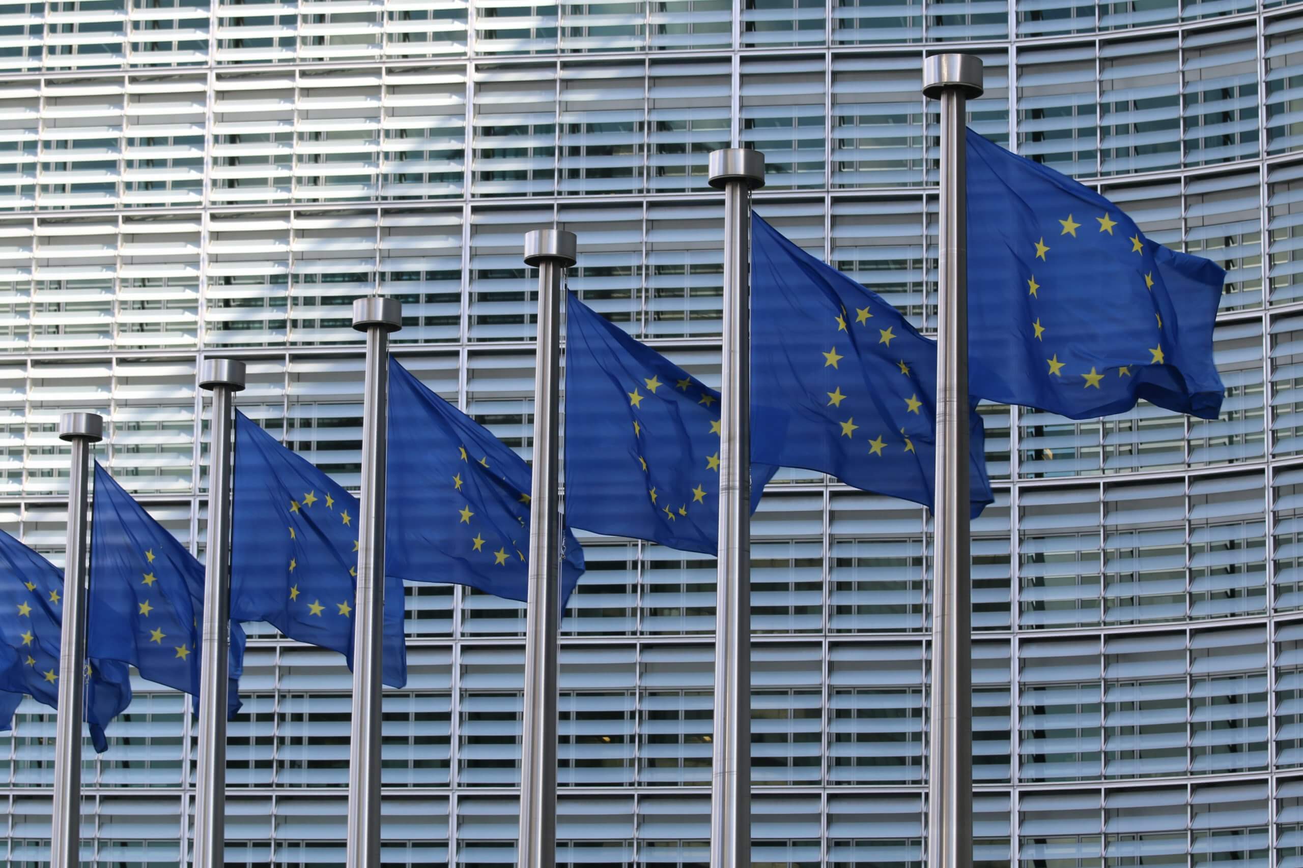 Multiple European Union flags with stars waving in front of modern office building exterior, representing cloud-based security compliance