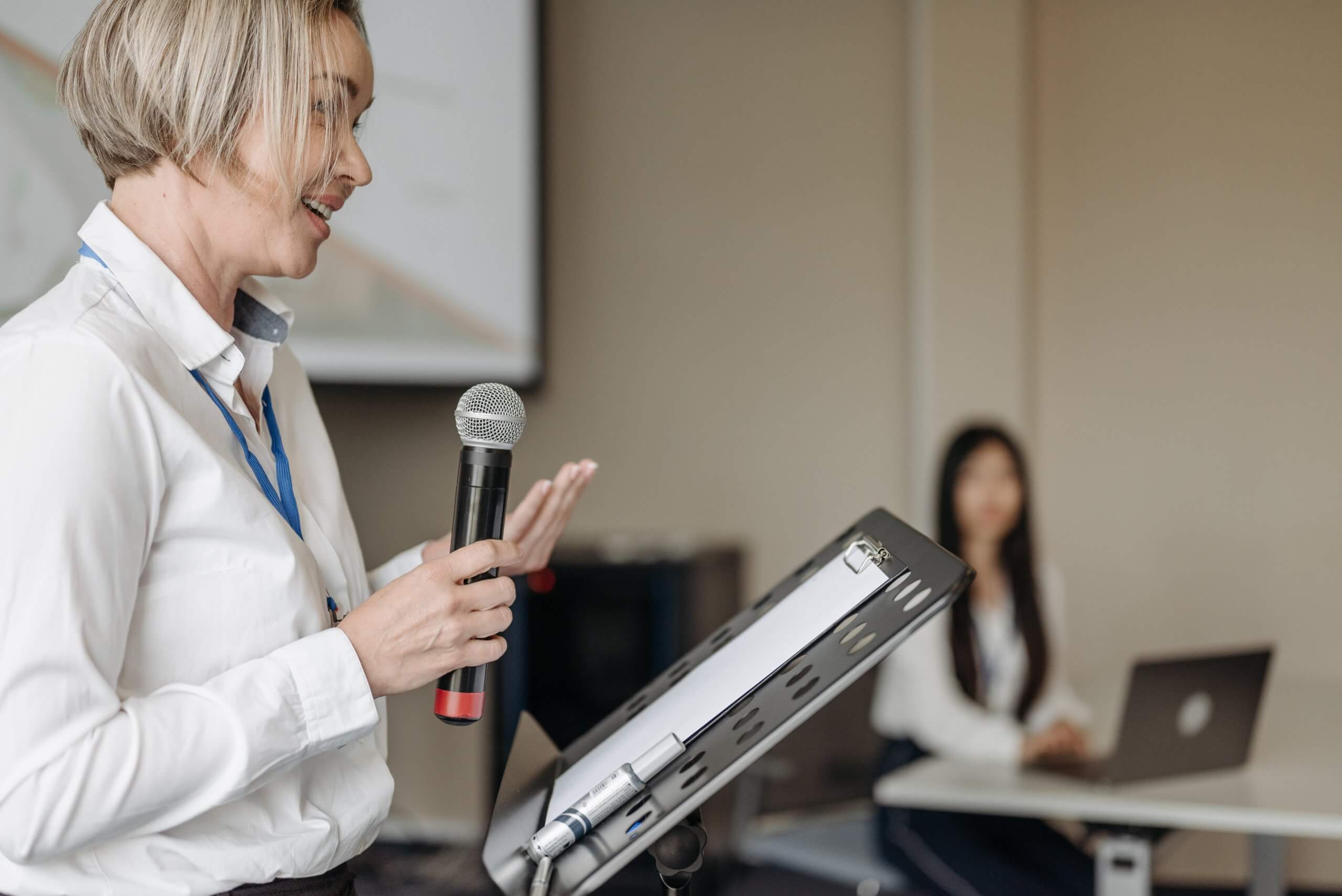 Professional presenter conducting workshop session with microphone and attendees present in training room environment